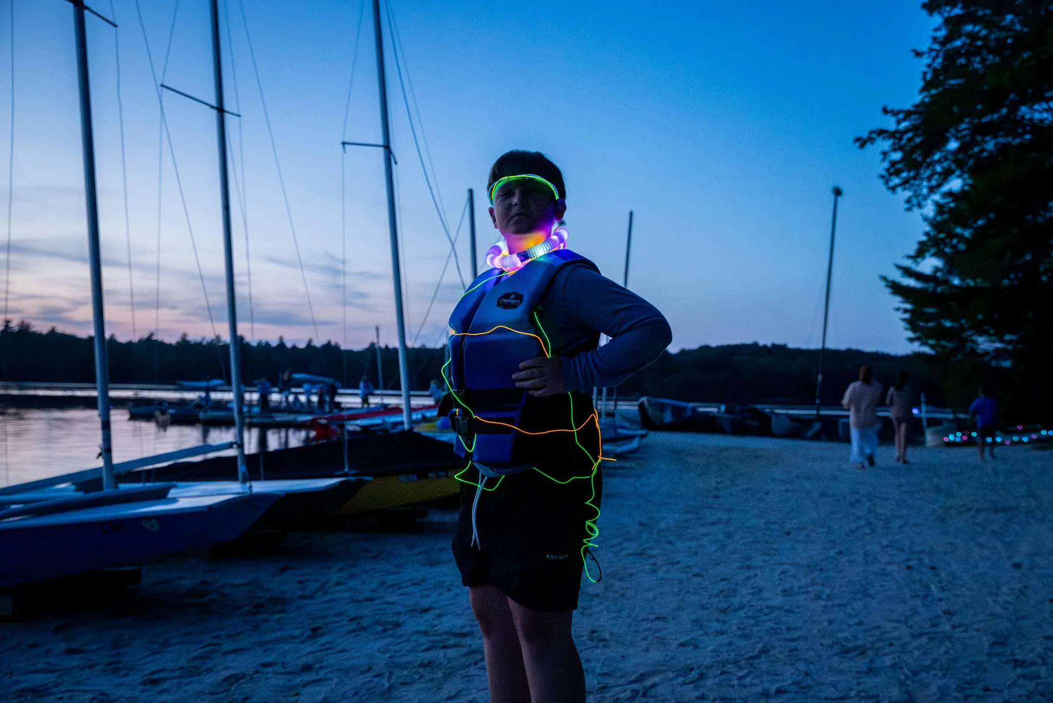Participant wearing glowing gear beside sailboats at dusk
