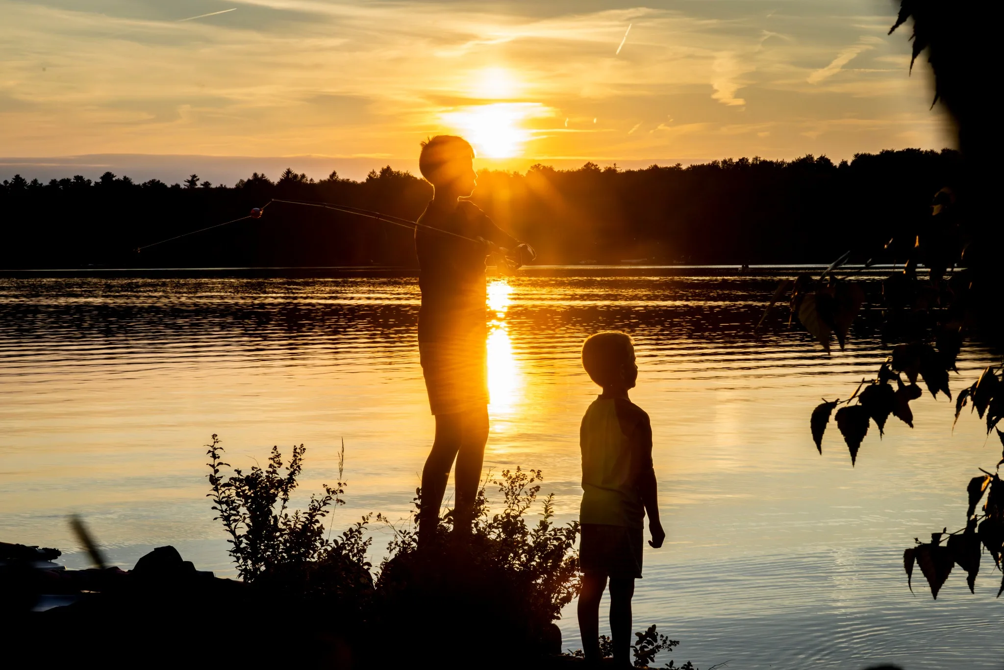 Two silhouetted figures at the edge of the lake at sunset