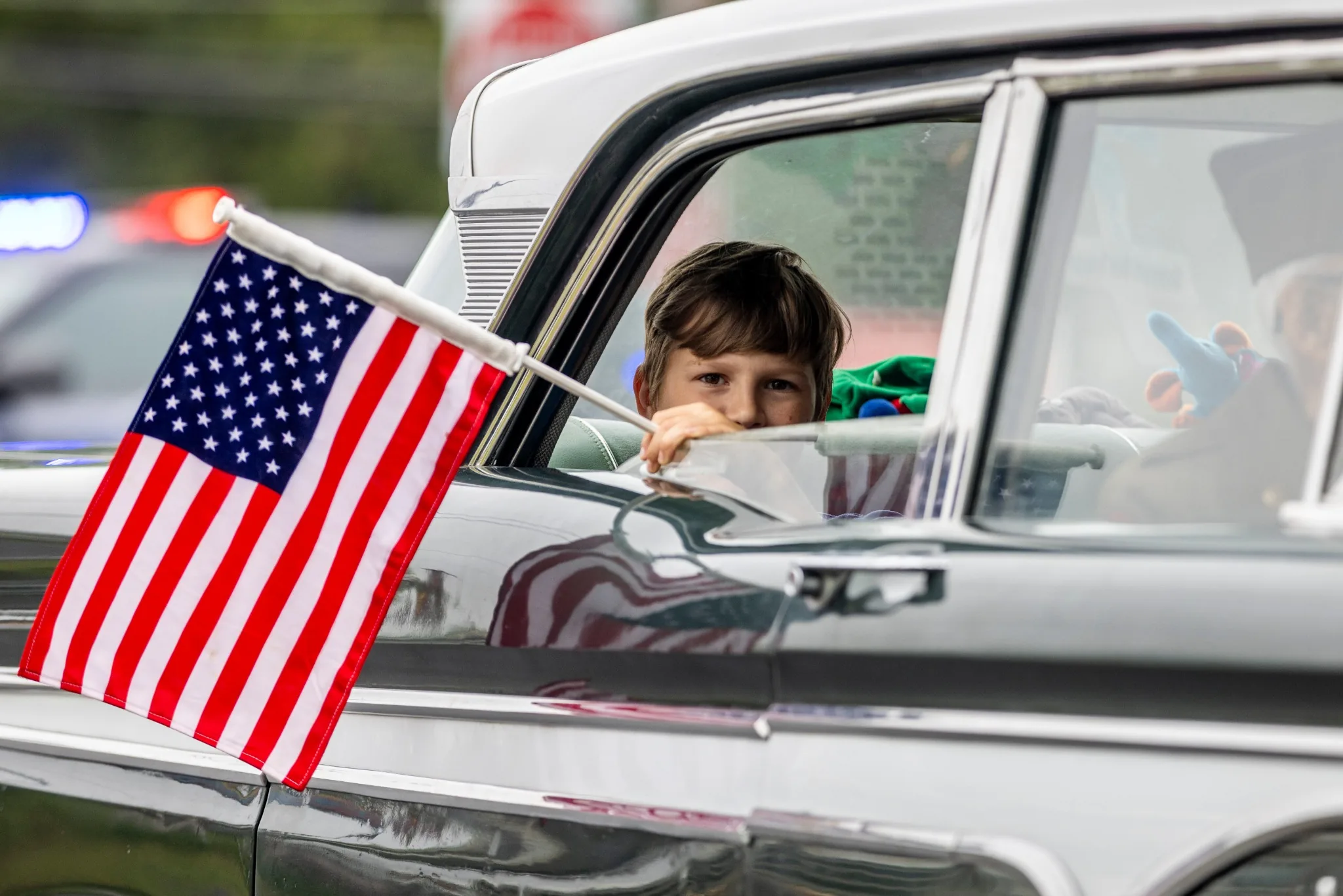Child framed by a car window behind an American flag during a community parade
