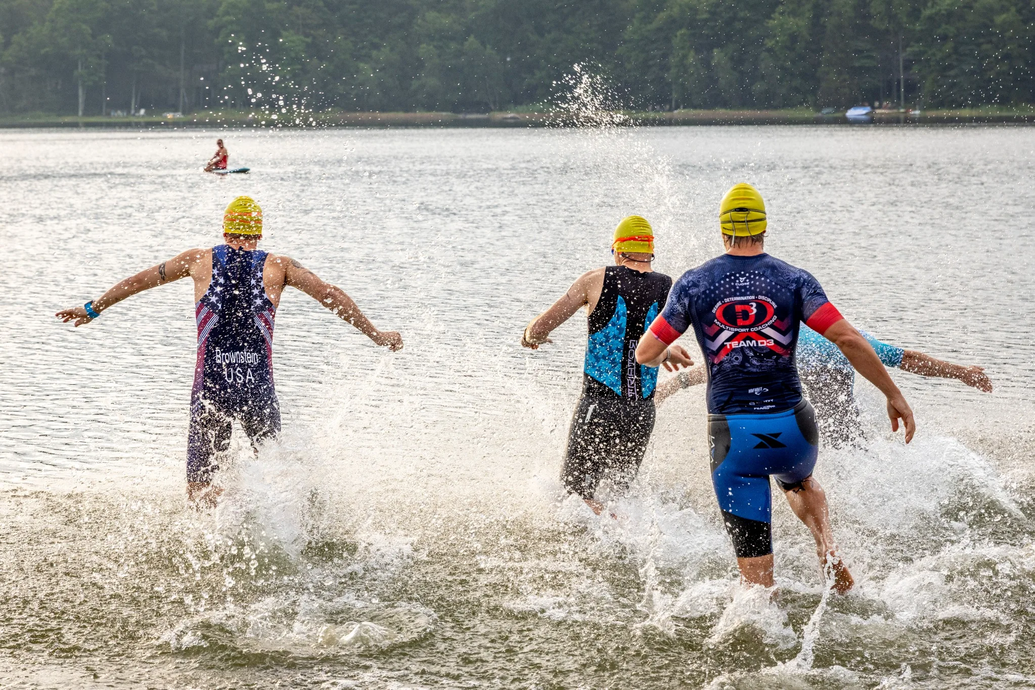 Triathletes running out of the lake through backlit spray